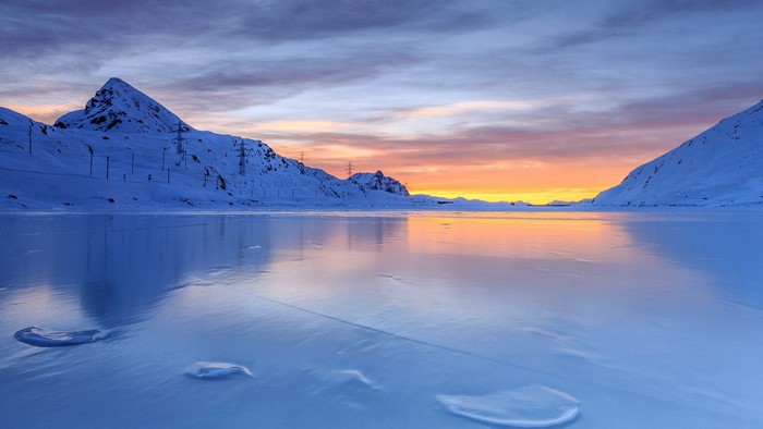 Sunset over a frozen lake in the Swiss Alps with mountains and power lines