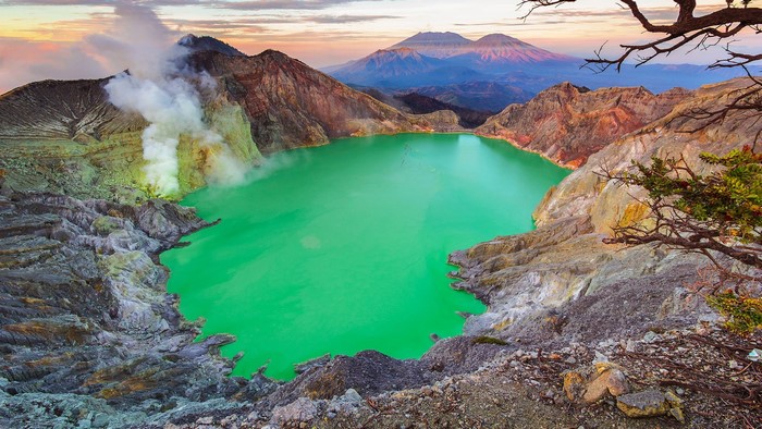 Mount Ijen volcano crater lake with smoke and mountains
