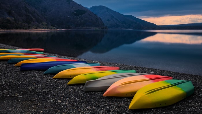 Colorful kayaks lined up on black sand beach at Lake Motosu, Japan