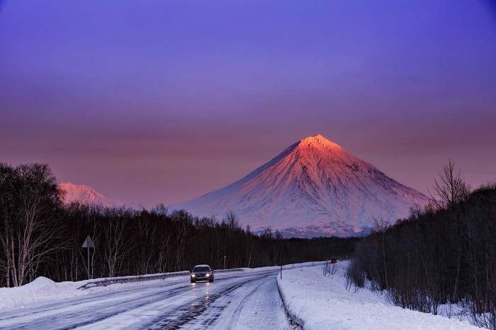 Car on snowy road with volcano at sunset