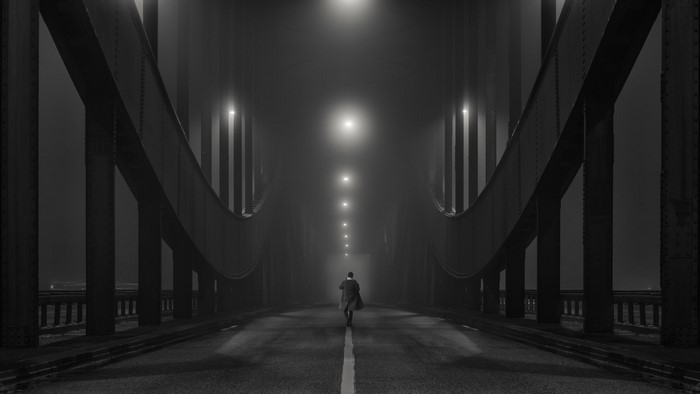 Man walking on a foggy bridge in Hamburg at night
