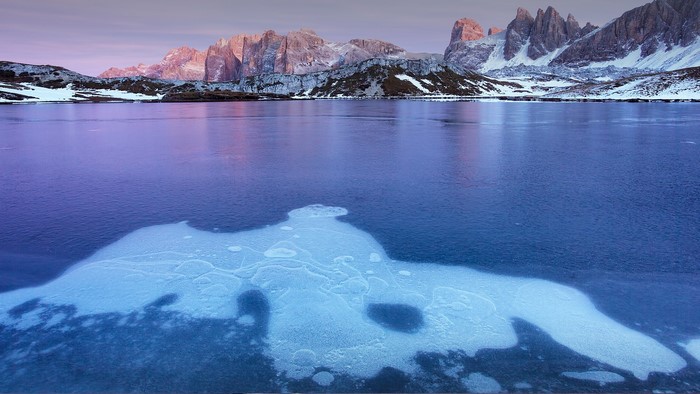 Frozen lake with snow-capped mountains at sunrise