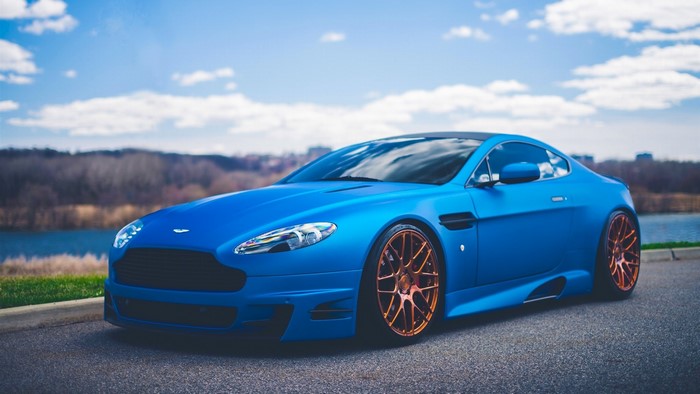 Blue Aston Martin Vantage with copper wheels on asphalt