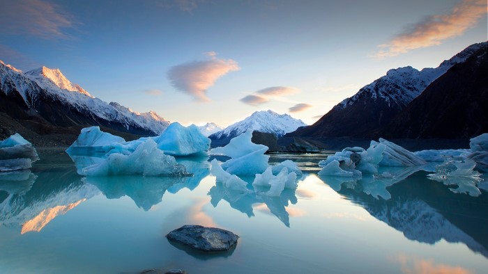 Icebergs in a lake with snowy mountains and sky reflection