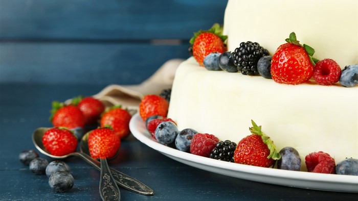 Two-tiered cake decorated with fresh berries and served with spoons