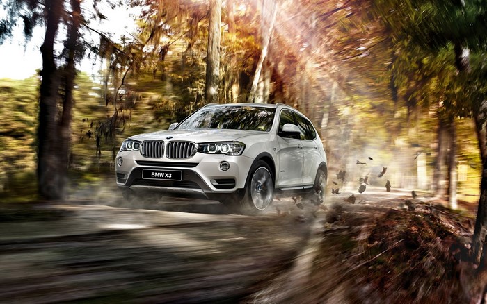 White BMW X3 driving on a dirt road through a forest