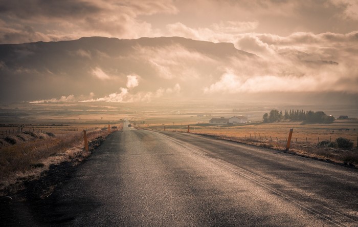 Asphalt road through a valley with mountains and clouds