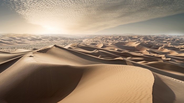Desert sand dunes at sunset with rippled sand and clouds