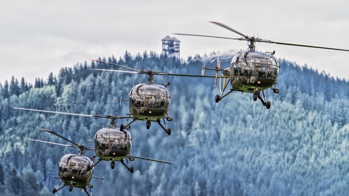 Four helicopters flying in formation over a forest