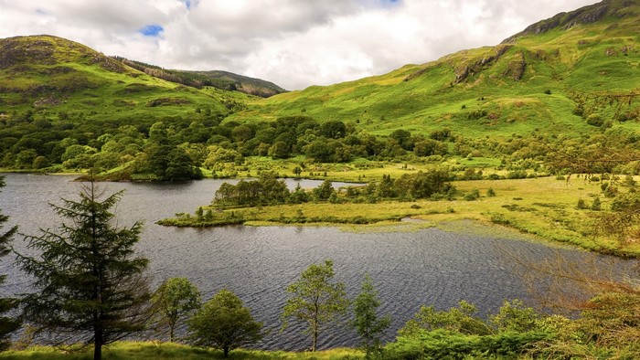 Green hills and lake landscape with trees and clouds