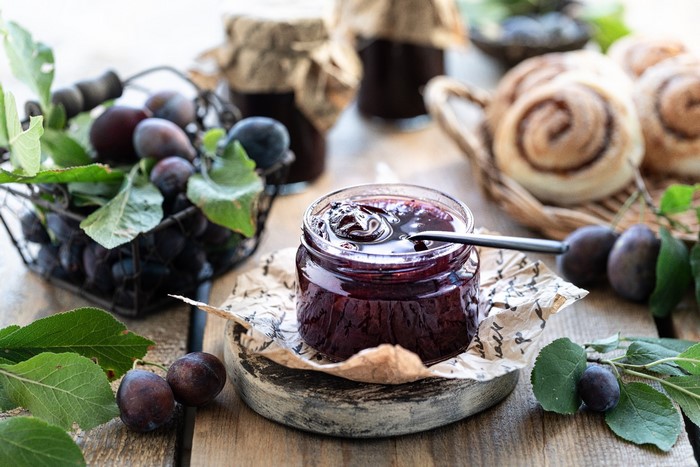 Plum jam in a jar with fresh plums and cinnamon rolls