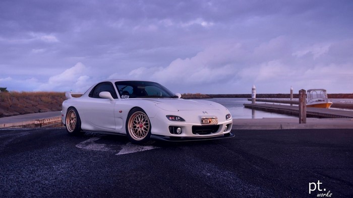 White Mazda RX-7 FD parked by a dock with boats