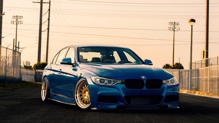 Blue BMW F30 with colored wheels on asphalt