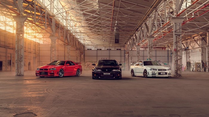 Three Nissan Skyline GT-R R34 cars in a warehouse