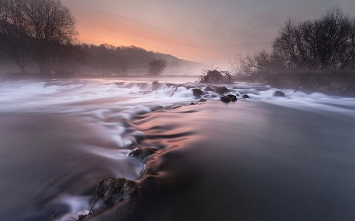 Misty river at sunrise with trees and rocks