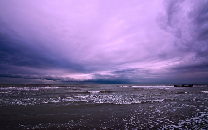 Stormy purple sky over a dark ocean with waves and a distant boat