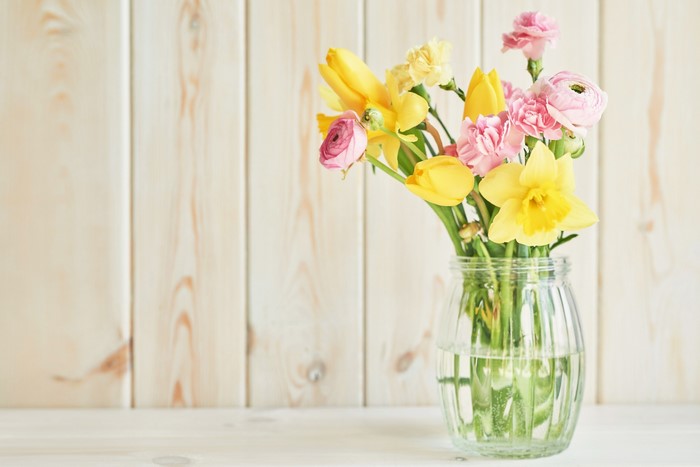 Bouquet of yellow tulips, daffodils, and pink carnations in a glass vase