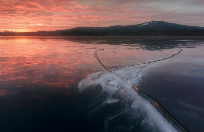 Frozen lake at sunset with mountains and cracked ice