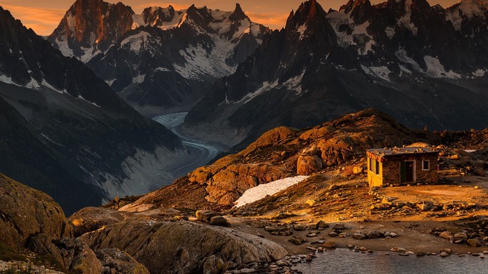 Small cabin on a rocky mountain slope with glacier and peaks