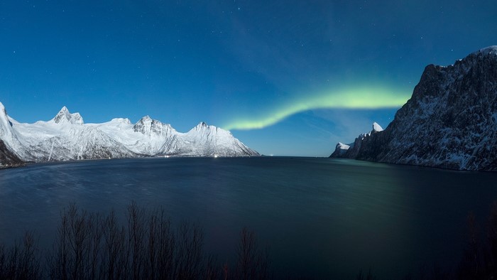 Aurora Borealis over snowy mountains and a lake in Norway