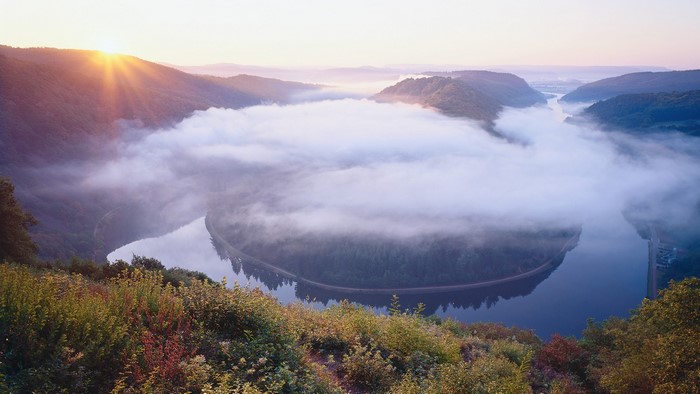 Misty river valley at sunrise with sun rays