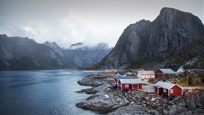 Red houses on rocky shore with mountains and water