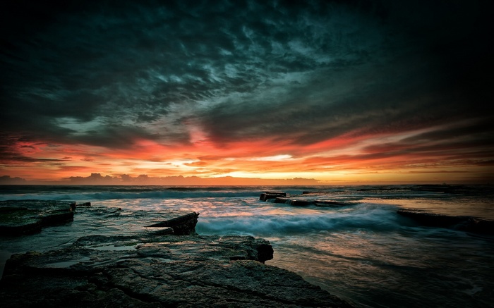 Dramatic sunset over rocky coastline with ocean waves