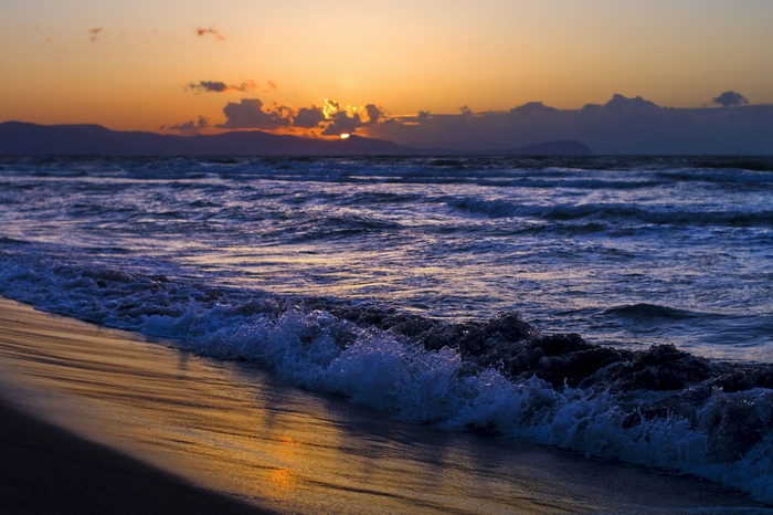 Sunset over the ocean with waves crashing on the beach