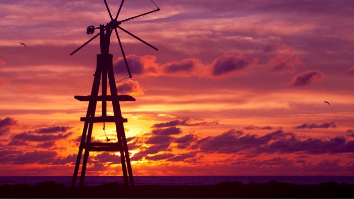 Silhouette of a windmill against a colorful sunset sky over the sea