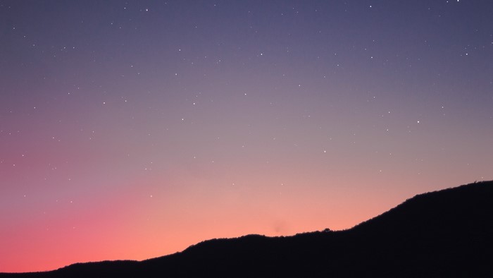 Silhouette of a mountain range against a starry twilight sky