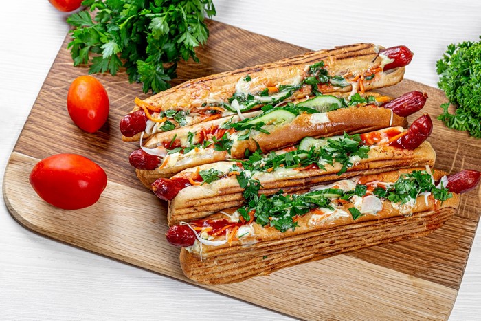 Four hot dogs with toppings on a wooden board
