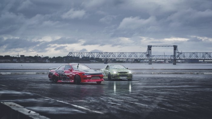 Two drift cars, red Nissan and green Toyota, on wet asphalt