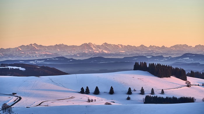 Snowy mountain landscape with trees and road at sunset