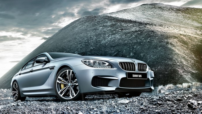 Silver BMW M6 parked on rocky terrain with mountain background