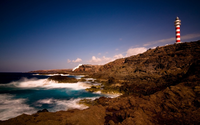Red and white lighthouse on a rocky coast with crashing waves