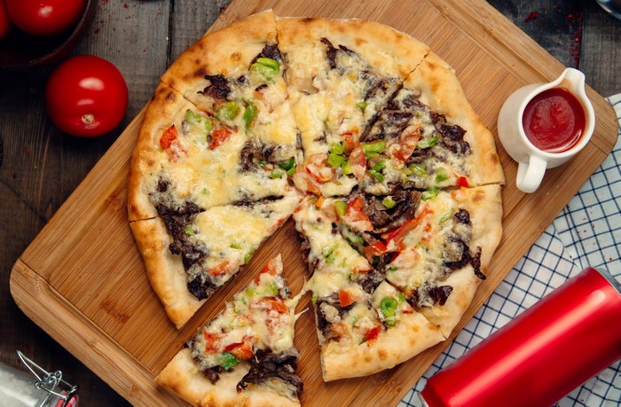 Pizza with cheese, meat, and tomatoes on a wooden board