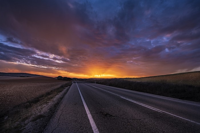 Asphalt road through fields at sunset with dramatic clouds