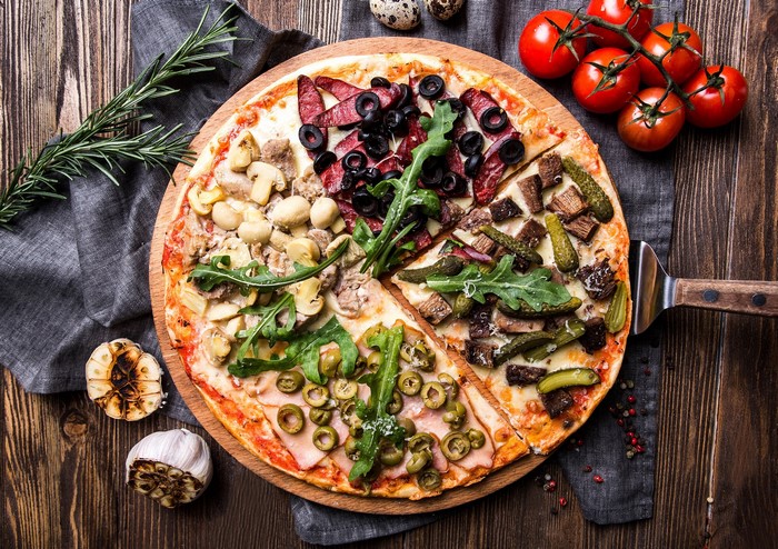 Four-section pizza with various toppings on a wooden board