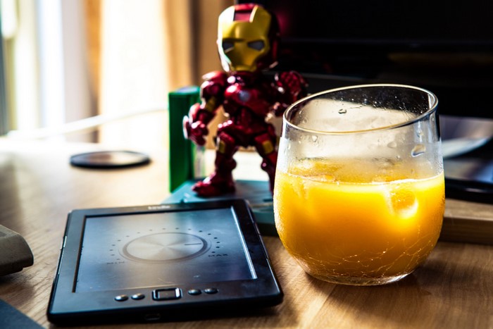 Iron Man toy, Kindle, and orange juice on a table