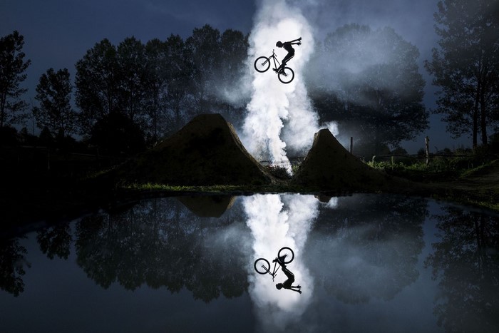 BMX rider performing a trick over water at night with smoke