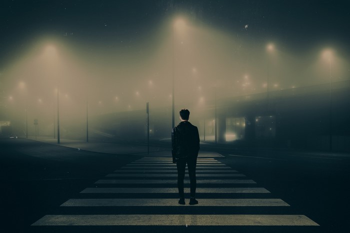 Man standing on a crosswalk at night in the fog