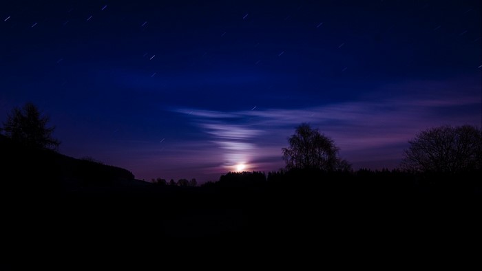 Night sky with moon and stars over silhouetted landscape