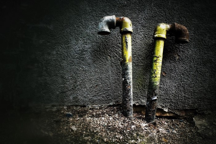 Two old, rusty pipes against a dark wall