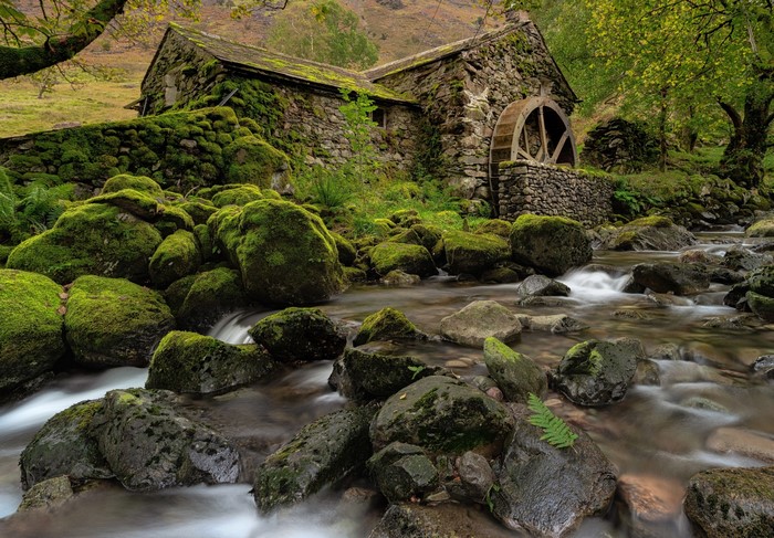 Moss-covered mill with water wheel by a rocky river in England