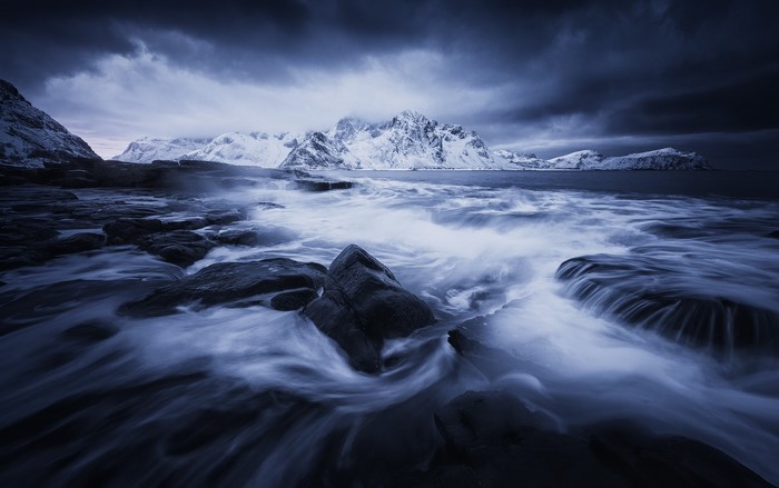 Waves crashing on rocks with snowy mountains in Lofoten