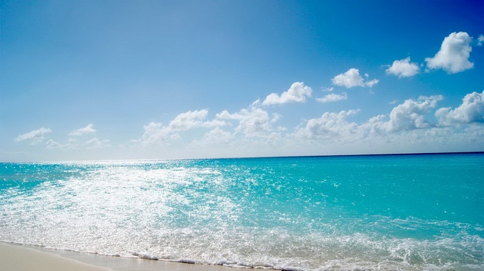 Turquoise ocean waves on a sandy beach under a blue sky