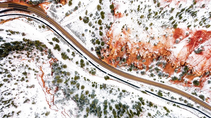 Aerial view of a snow-covered road through red rock formations and trees