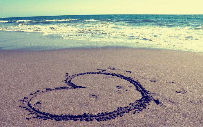 Heart drawn in sand on a beach with ocean waves