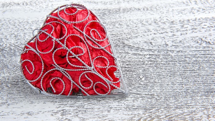 Red heart-shaped box filled with crumpled paper on wood