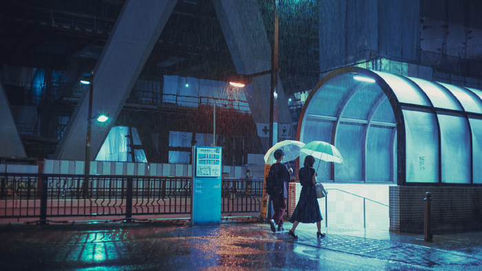 Two people with umbrellas walk in the rain at night in Japan